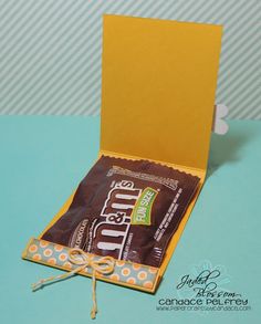 a candy bar in a yellow box on a blue table with an orange bow around it