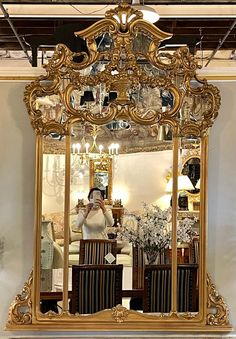 a woman taking a selfie in front of a large mirror with chairs and chandelier