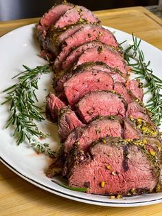 sliced roast beef on a white plate with sprigs of rosemary and seasoning