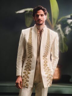 Step into refined elegance with the Kaju Katli Raja koti, an opulent sherwani adorned with intricate gold zardozi, katdana, and pearl embroidery, inspired by 'Berry Bel'. The ensemble includes a short georgette tissue kurta that adds a playful touch and straight, tailored pants for a smart finish. This piece is a perfect blend of grandeur and modern sophistication. Elegant Traditional Wear With Gota Work For Festivals, Elegant Traditional Wear With Gota Work For Designer Wear, Elegant Traditional Wear With Gota Work For Reception, Elegant Traditional Wear With Gota Work, Elegant Raw Silk Sherwani With Traditional Drape, Elegant Traditional Wear With Gota Work For Diwali, Beige Set With Intricate Embroidery And Traditional Drape, Elegant Dola Silk Kurta For Reception, Gold Chanderi Sherwani For Wedding