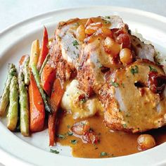 a white plate topped with meat and veggies covered in gravy next to asparagus