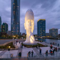 a large white statue in the middle of a city at night with people walking around