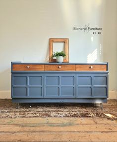 a blue dresser sitting on top of a wooden floor next to a mirror and potted plant