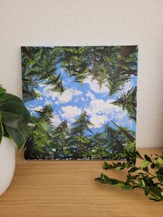 a painting on a wooden table next to a potted plant and a white vase