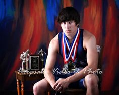 a young man sitting in a chair with two trophies and a plaque around his neck