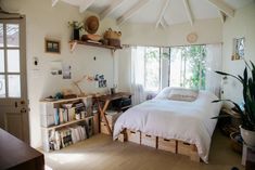 a bed sitting in a bedroom next to a wooden table and bookshelf on top of a hard wood floor