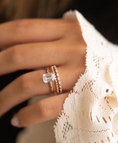 a woman's hand with two rings on top of her finger and an engagement ring in the middle