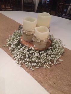 two white candles sitting on top of a wooden stand filled with baby's breath flowers