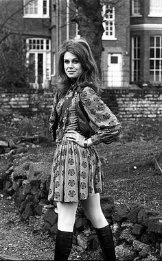 a woman standing in front of a brick building with her hands on her hips and wearing knee high boots