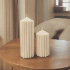 two white candles sitting on top of a wooden table