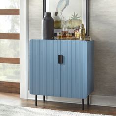 a blue cabinet sitting in front of a window next to a vase and other items