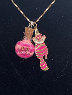 two pink and gold necklaces with cats on them, one is in a bottle