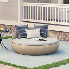 an outdoor day bed with pillows on it in front of a patio table and chair