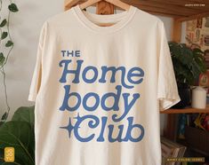 "The Homebody Club" Unisex T-shirt Design by jojoyu This item is made to order. If you want an oversized fit please size up! for reference, the model on the photo is usually a medium but wearing XL for an oversized fit. About the shirt: ◦ color: ivory ◦ relaxed fit  ◦ soft-washed, garment-dyed fabric ◦ double-needle stitching throughout the tee makes it highly durable  ◦ made with medium fabric (6.1 oz/yd²) consisting of high quality, 100% ring-spun US cotton for long-lasting comfort ◦ made with Fall Tees For Women, Trendy Vinyl Shirt Ideas, Popular Tshirt Designs 2024, Simple Graphic Tees Design, Cute Shirt Ideas Vinyl, The Homebody Club, Tshirt Design Ideas Trendy 2024, Oversized Dress Shirt Outfit, T Shirt Ideas Design