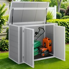 an outdoor storage shed with lawn mowers in the back ground and grass surrounding it