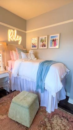 a white bed sitting next to a wall with pictures on the wall and a footstool in front of it