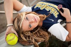 a woman laying on a bench with a softball in her hand and looking at the camera