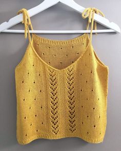 a yellow knitted top hanging on a white hanger next to a gray wall