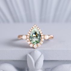 an engagement ring with a green and white stone surrounded by pearls on a white surface