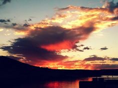 the sun is setting over some water and hills in the distance with clouds above it