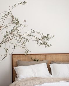 a bed with white linens and pillows in front of a plant on the wall