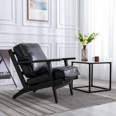 a black leather chair sitting next to a table with a vase on top of it