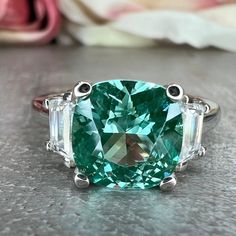 "The ring pictured is lab created green paraiba with moissanite accents #6778 This ring can be made with many different stone colors Message us for pricing on different color/type stones -Approximate total carat weight:  2.80ctw diamond equivalent  -Center Stone Size: 8x8mm - approx. 2.40ct diamond equivalent -Gem Type:  lab created Green Paraiba -Center Stone Shape:  Cushion cut  -Center Stone Color: green (mint green) -Center Stone Clarity: VS2 -Moh's Scale: 7.5 - 8 hardness -Side Stone Size: Paraiba Tourmaline Ring, Jewellery Board, Ring Three Stone, Paraiba Tourmaline, White Gold Set, Green Mint, Ring Pictures, Tourmaline Ring, Mothersday Gifts