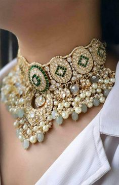 a woman wearing a gold and green choker with pearls on the bottom, surrounded by jewels