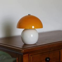 an orange and white lamp sitting on top of a wooden table next to a dresser