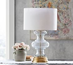 a table lamp sitting on top of a white table next to a vase with flowers