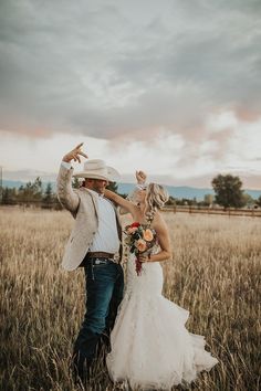 a bride and groom are standing in the middle of a field with their arms up