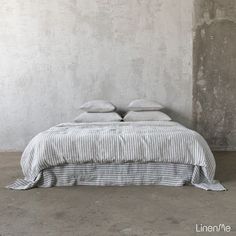 a bed with two pillows sitting on top of it next to a wall and cement floor