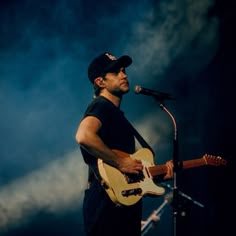 a man holding a guitar while standing in front of a microphone on top of a stage