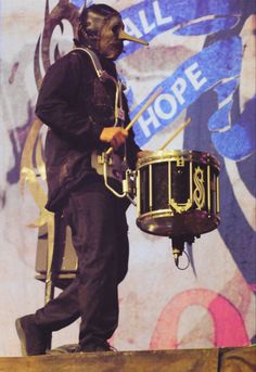 a man with a mask on holding a drum