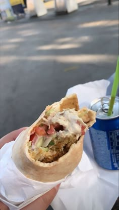 a person holding a burrito in their hand with a soda on the other side