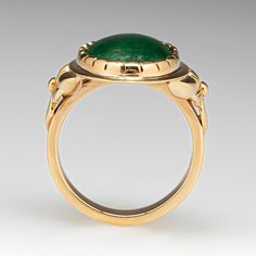 This wonderful ring is centered with one (1) oval cabochon cut natural jadeite jade set into a closed back scalloped bezel setting. Engraved floral details accent the shoulders of the ring. The ring measures 20.6mm at the top, rises 5.9mm above the finger, tapering to 3.5mm wide and 1.6mm thick at the base of the shank. This ring is currently a size 7. The jade shows overall wear on the surface. Formal Emerald Cabochon Ring, Formal Oval Cabochon Emerald Ring, Elegant Green Intaglio Ring, Formal Oval Cabochon Emerald Ring With Bezel Setting, Classic Oval Chrysoprase Ring, Elegant Oval Chrysoprase Rings, Elegant Emerald Jade Ring With Cabochon, Formal Oval Jade Emerald Ring, Yellow Gold Jade Cabochon Ring