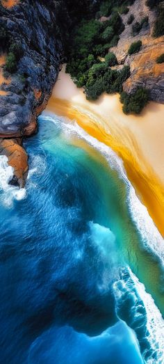 an aerial view of the ocean and beach with yellow sand, blue water and green trees