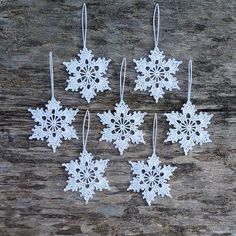 six snowflake ornaments hanging from strings on a wooden surface