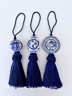 three tasseled ornaments with blue and white designs hanging from strings on a white background