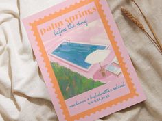 a pink book with an image of a swimming pool on the cover and some dry grass next to it