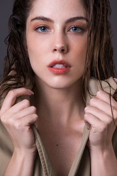 a woman is posing with her hands on her chest and wearing a trench coat over her shoulders