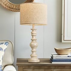 a lamp sitting on top of a wooden table next to a white chair and mirror