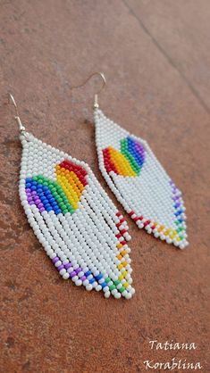 a pair of white beaded earrings with multicolored tears on top of a brown surface