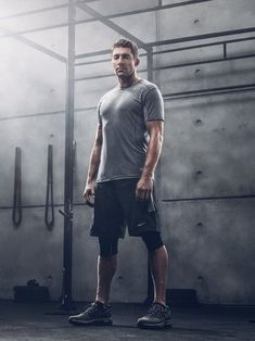 a man in grey shirt and black shorts standing next to a metal rack with gym equipment