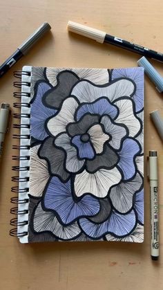 a spiral notebook with an abstract flower design on it next to crayons and markers