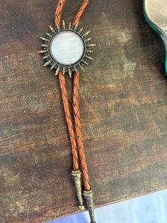 This awesome bolo tie has a southwestern brass sun design and pearl white stone centerpiece. The cord is brown genuine leather. Our bolos pair nicely with many of our belt buckles! They make wonderful gifts. The western bolo tie rope length is 39'' ; charm pendant size is 1 1/2'' Adjustable Gold Western Bolo Ties, Gold Western Bolo Tie, Adjustable Brown Western Jewelry, Adjustable Concho Bolo Ties For Ranch, Western Style Adjustable Bolo Ties, Brown Concho Jewelry For Rodeo, Western Style Brown Jewelry With Adjustable Length, Brown Western Jewelry With Adjustable Length, Brown Western Jewelry With Adjustable Cord