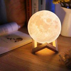 the moon lamp is sitting on top of a table next to a book and some books