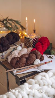 balls of yarn and knitting needles sit on a table next to a christmas tree with lights in the background