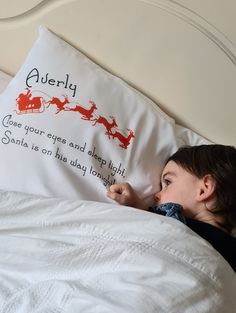 a little boy laying in bed with a pillow that has santa's sleigh on it