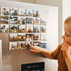 a young boy pointing at pictures on a wall with magnets in front of him